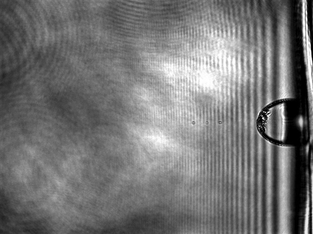 A micro bullet traveling at supersonic speed is captured in this composite of three timed images, as it makes its way toward a suspended sheet of multilayer graphene. Experiments carried out at Rice University show graphene is 10 times better than steel at absorbing the energy of a penetrating projectile. The bubble at left is a polymer film expanding away from the gold substrate that transfers energy from a laser to the micro bullet.