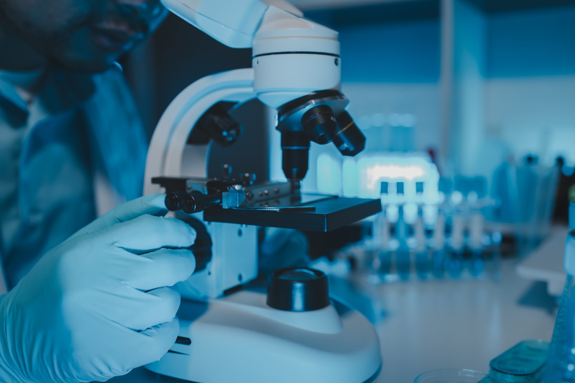 Gloved scientist adjusting a microscope in a laboratory.