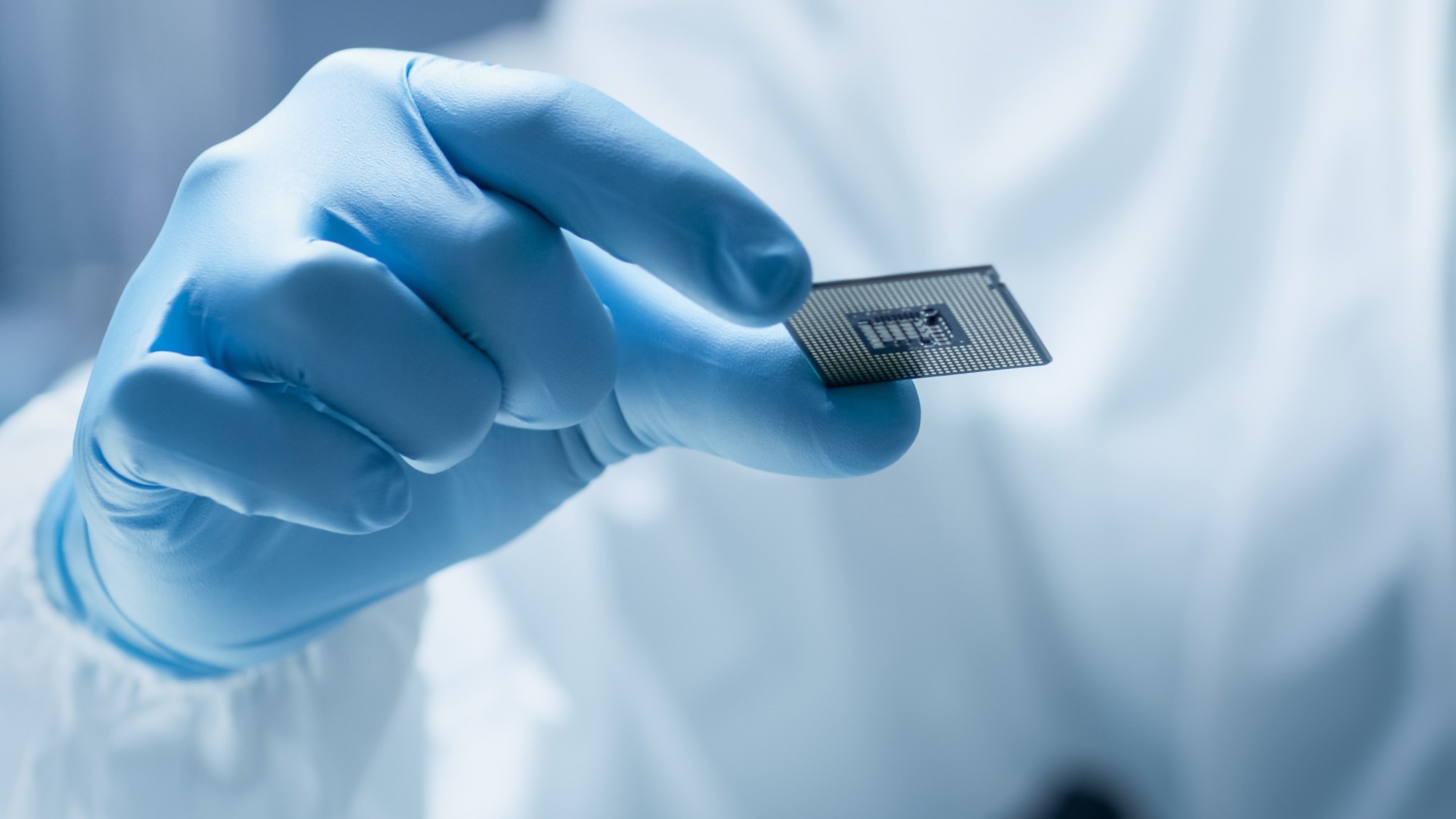 In Ultra Modern Electronic Manufacturing Factory Design Engineer in Sterile Coverall Holds Microchip with Gloves and Examines it.