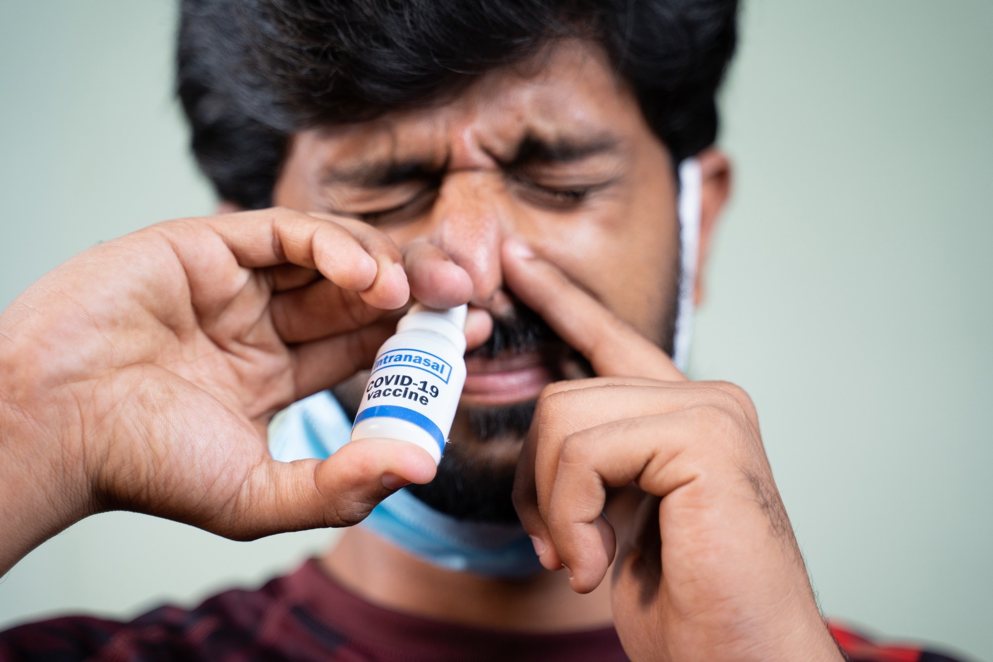 Close up head shot of young man inhaling coronavirus covid-19 nasal spray