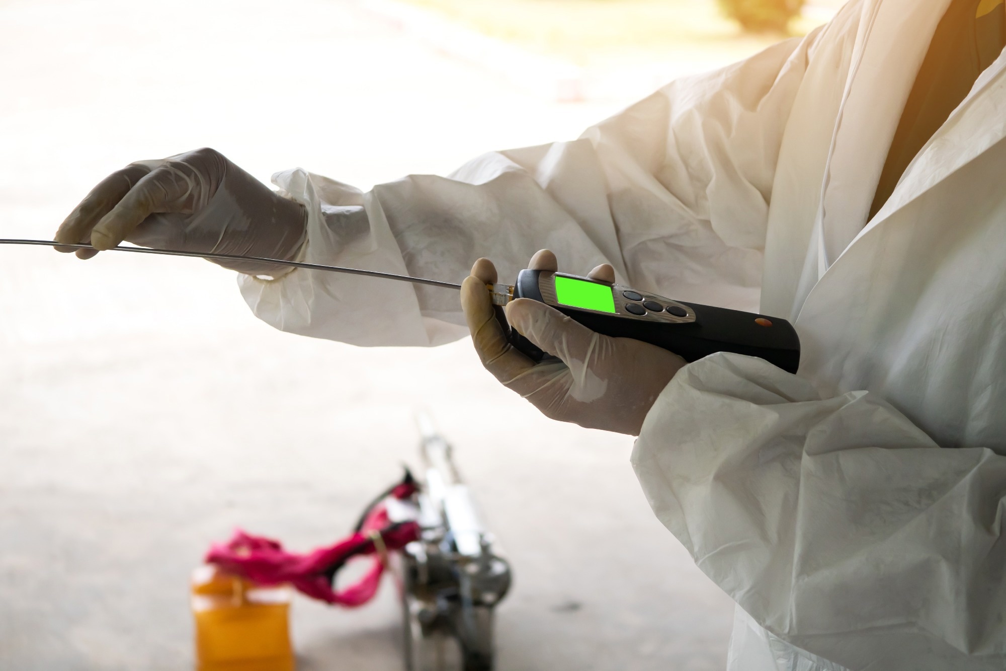 Person in protective clothing using a handheld air quality detector to measure gases or VOCs in an industrial setting.