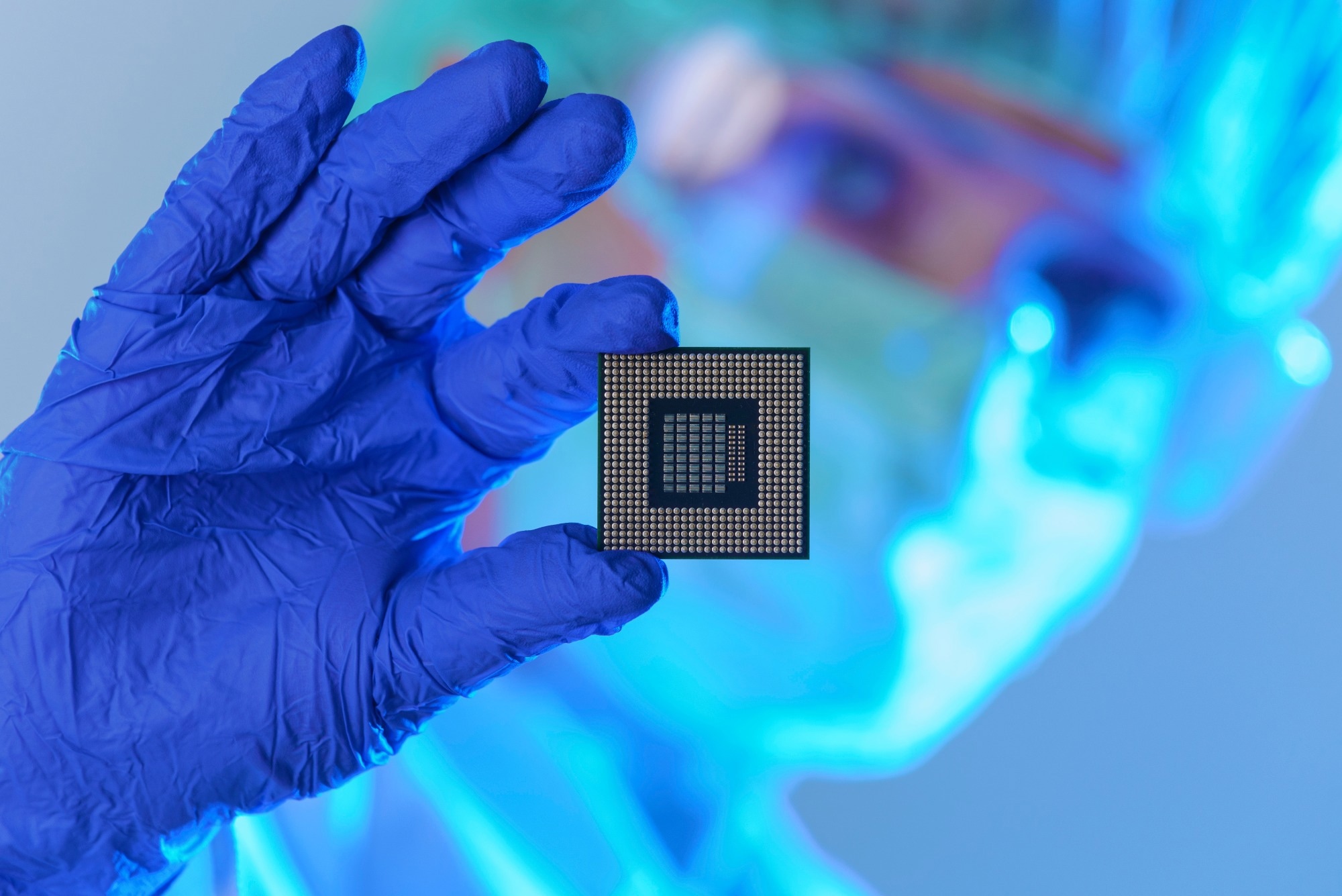 An engineer working in a laboratory wearing a special uniform and protective gloves holds new processor in hands and examines it