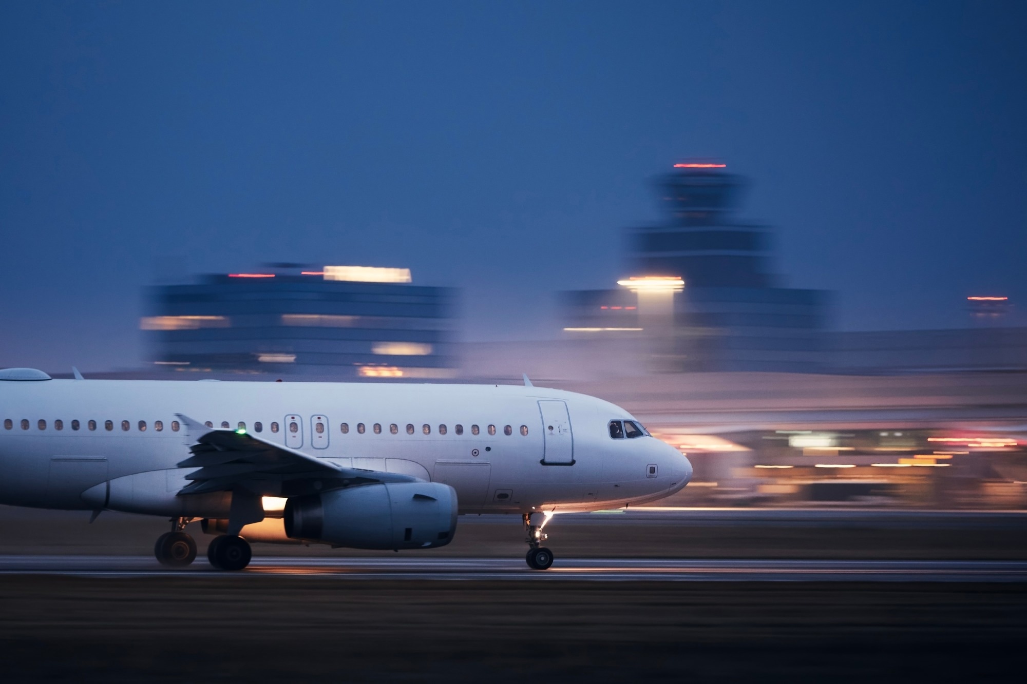 Airplane during take off on runway at night against air traffic control tower. Plane in blurred motion at night.