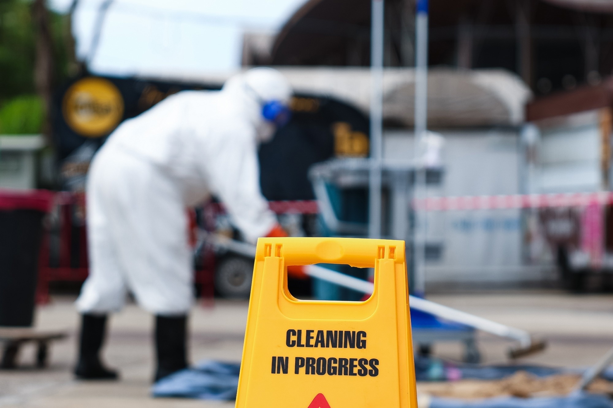 Cleaning in progress sign with a worker in a protective suit clearing an area.