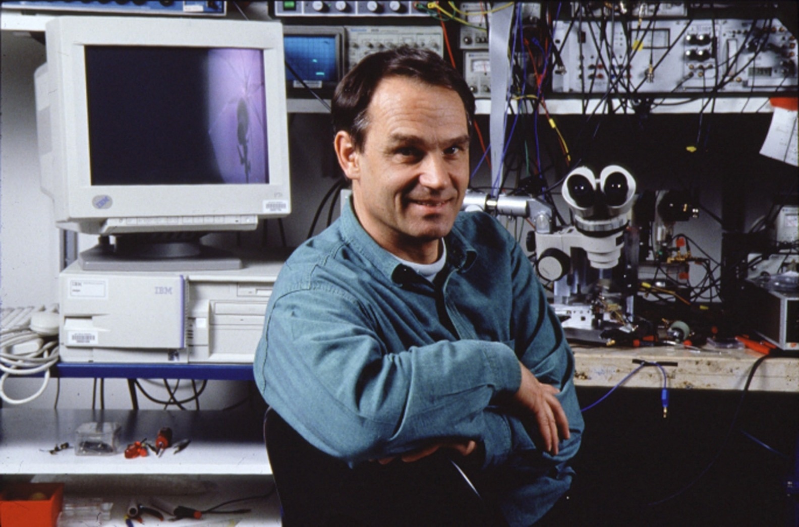 An image of Gerd Binnig turning towards a camera, with computer and instrumentation behind him. Rights obtained from IBM Zurich.