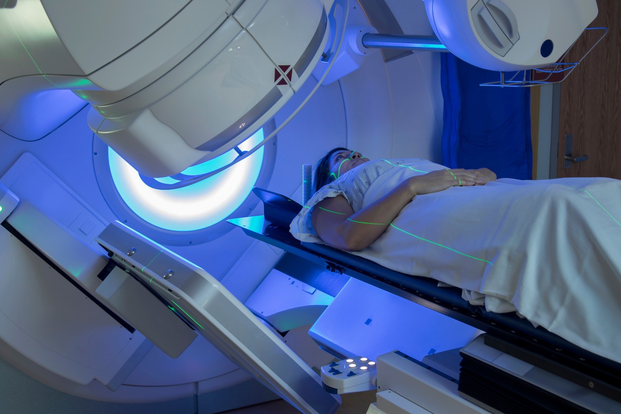 A woman lies on the bed of a radiotherapy instrument.