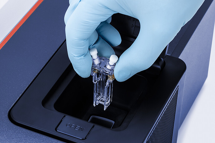 A scientist wearing blue nitrile gloves place a sample into the Litesizer analytical compartment.