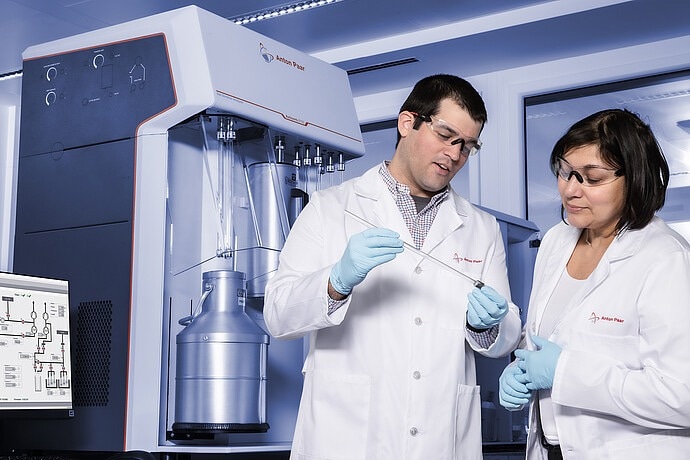 Two scientists review a glass item for use with the Autosorb. The man and woman wear lab coats and goggles.