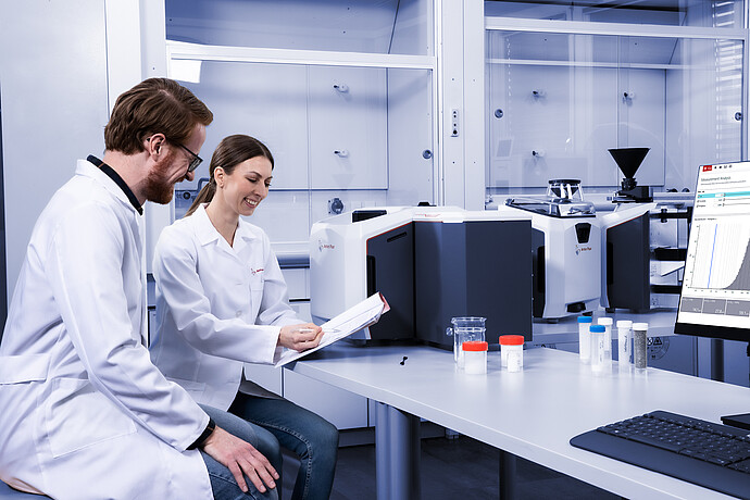 Two people in white lab coats sit smiling at a sheet of paper with the Litesizer DIA in the background.