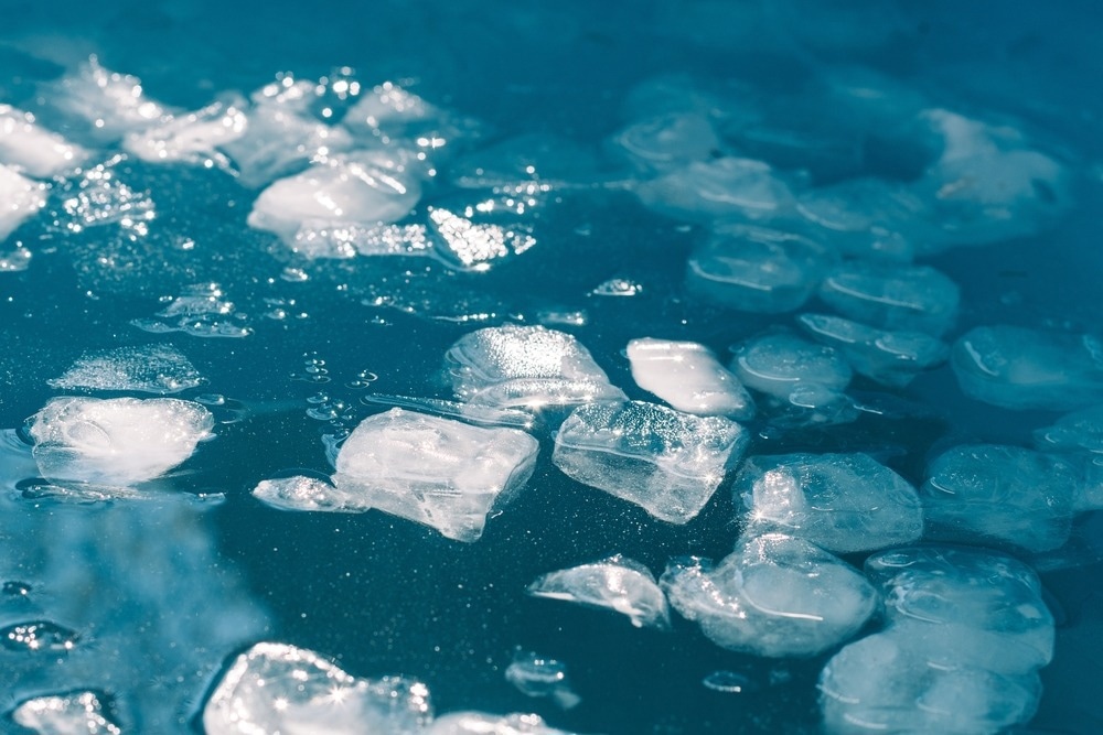 Cold water and ice cubes melting under the sun background.