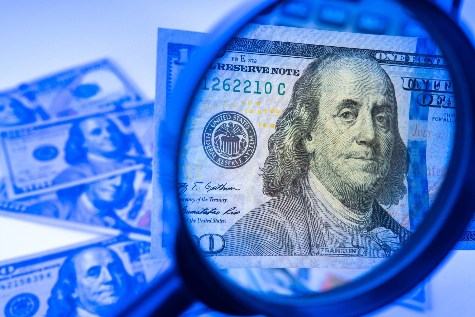 Counterfeit money. A hundred-dollar bill is studied with a magnifying glass. Money in the ultraviolet light.