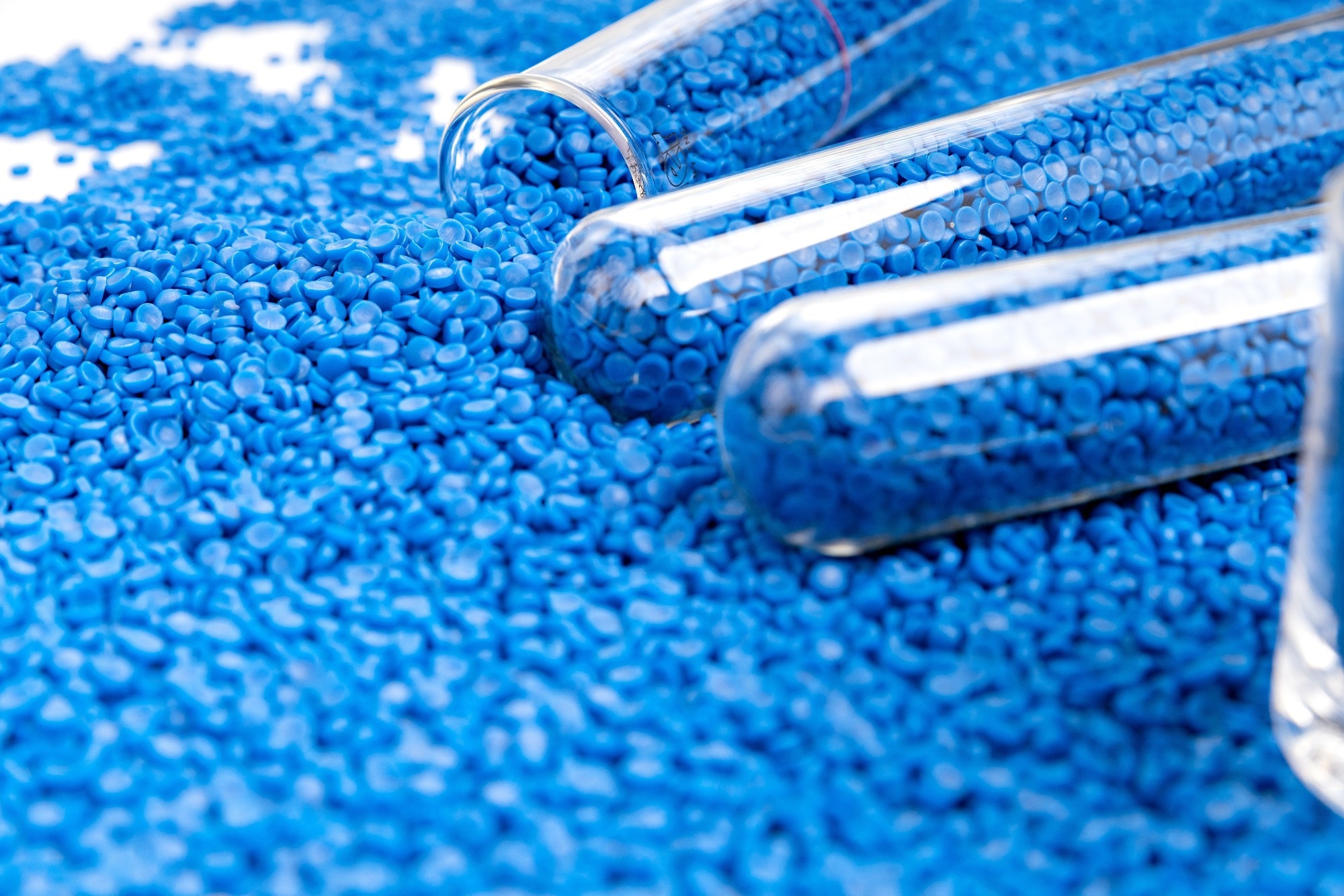 Close-up of bright blue polymer microbeads scattered around transparent test tubes