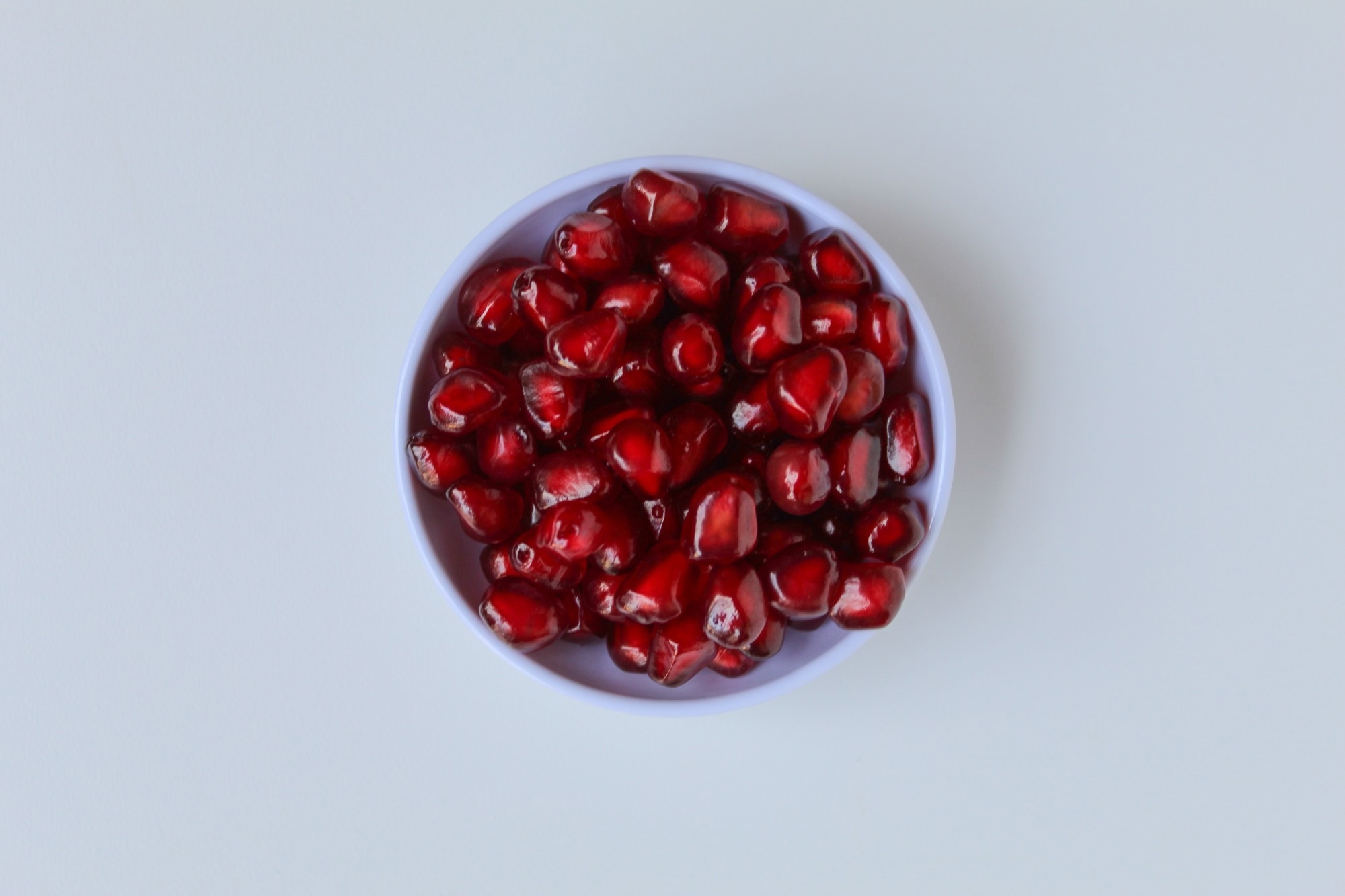Fresh red seeds of pomegranate fruit, in small bowl, isolated on white background, flat lay or top view