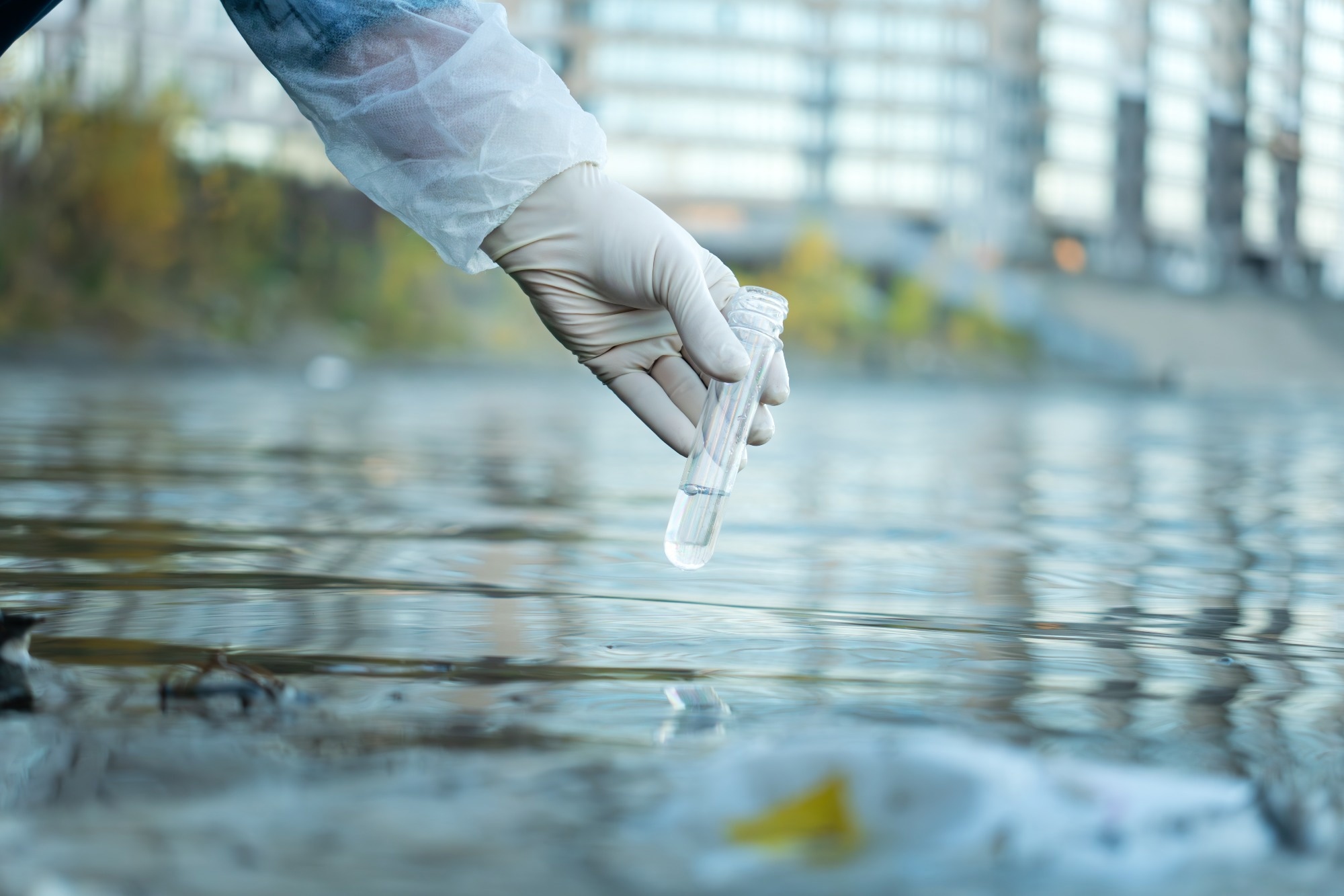 Close up of scientist with white glove holding test tube with water in his hand.