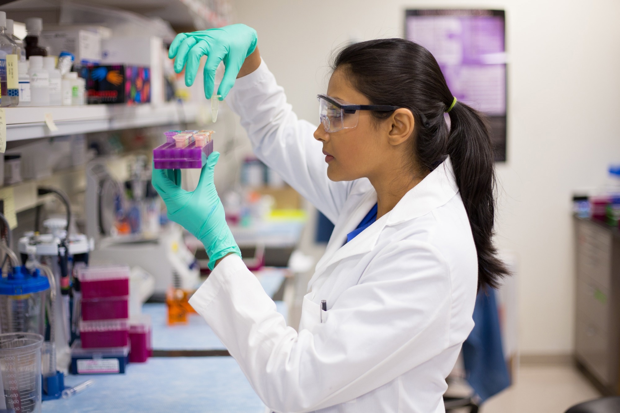 A scientist assesses her samples in the light, wearing a lab coat and green nitrile gloves.