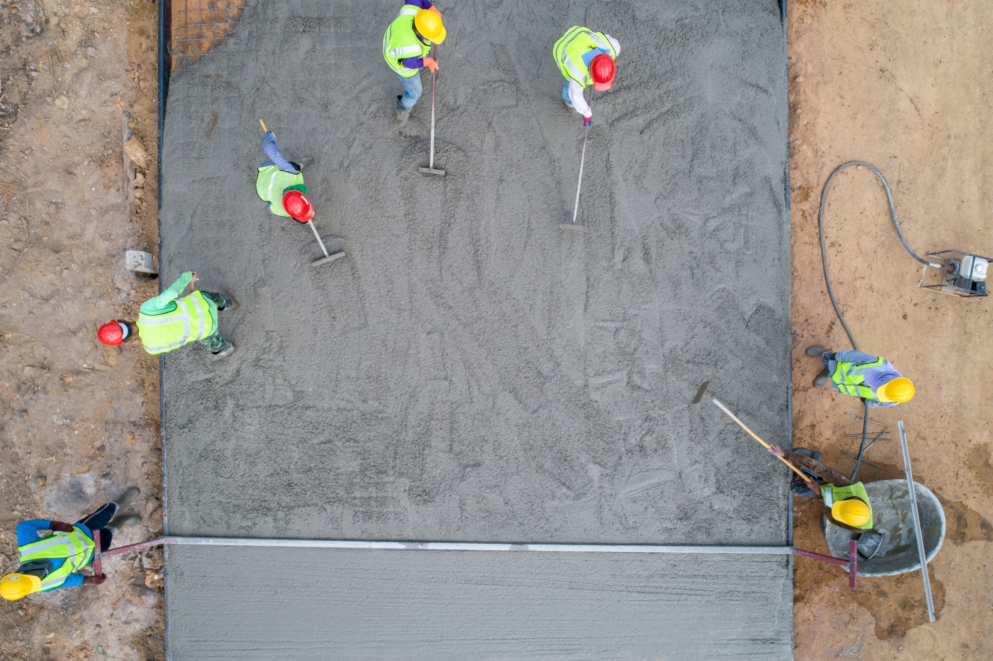 Construction workers spreading concrete on a building site, wearing different coloured helmets and hi-vis jackets.