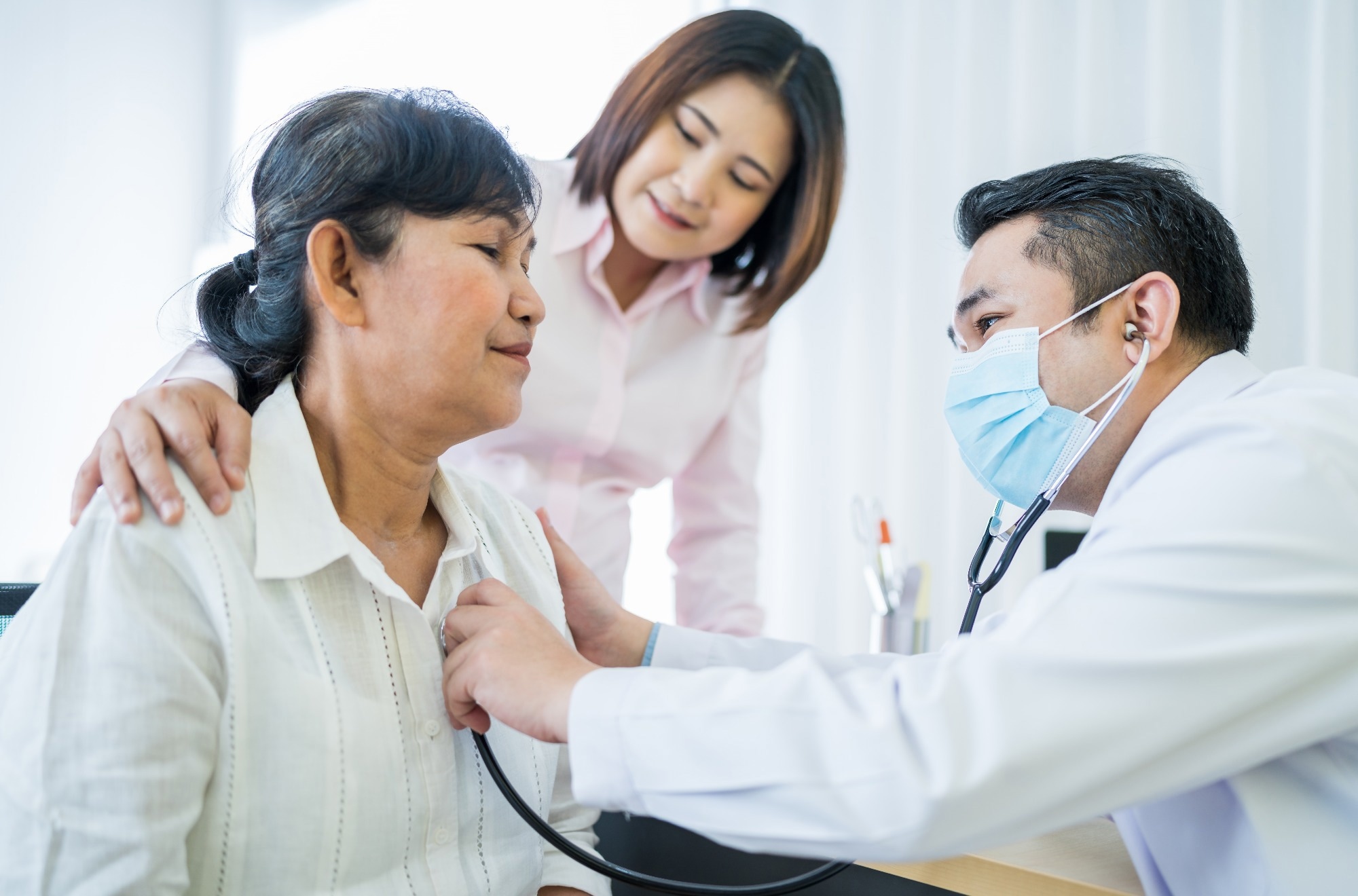 A doctor examines an older woman, using a stethoscope to monitor her breathing.