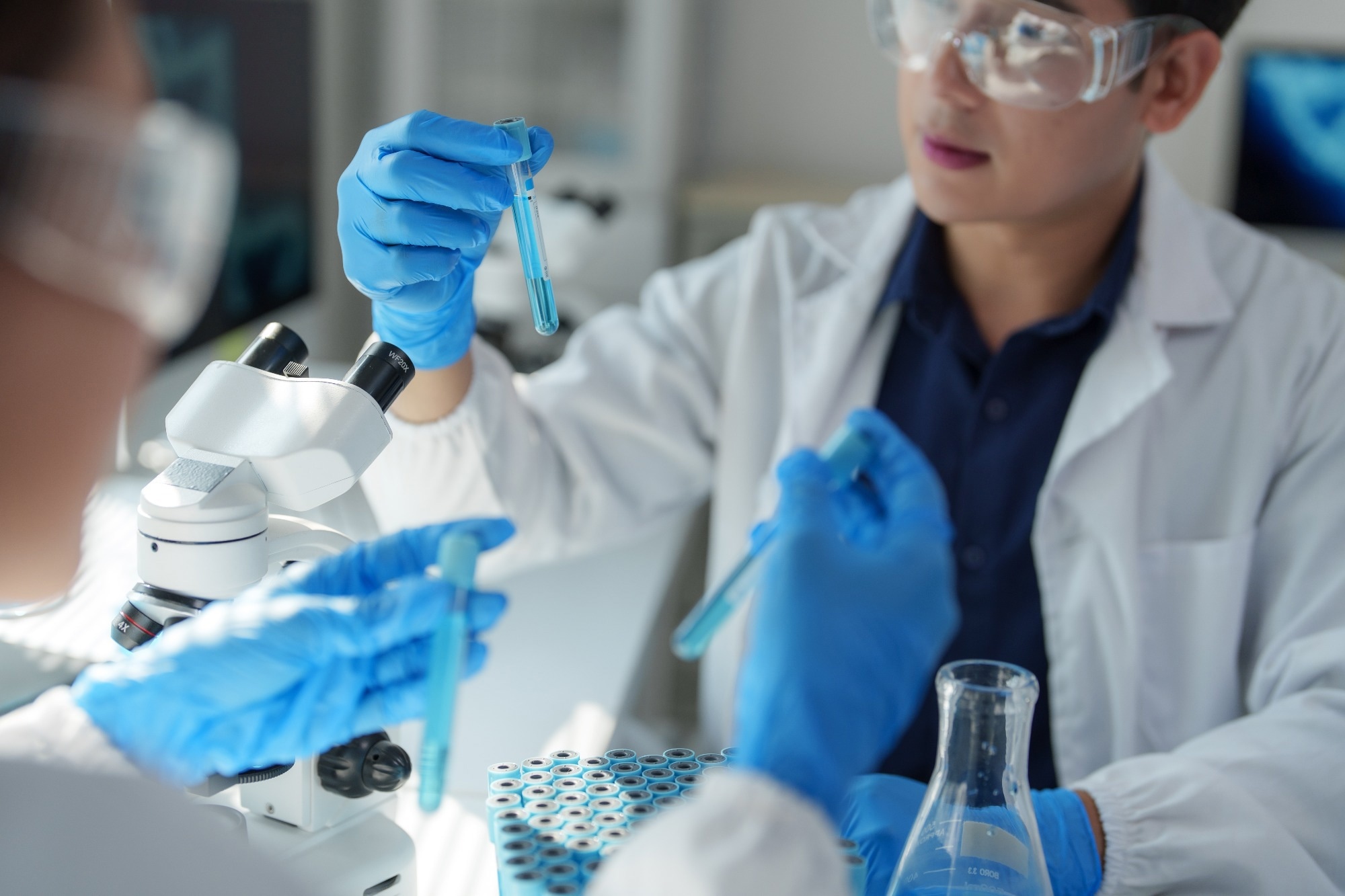 Two scientists reviewing blue sample liquid, wearing blue vinyl gloves.