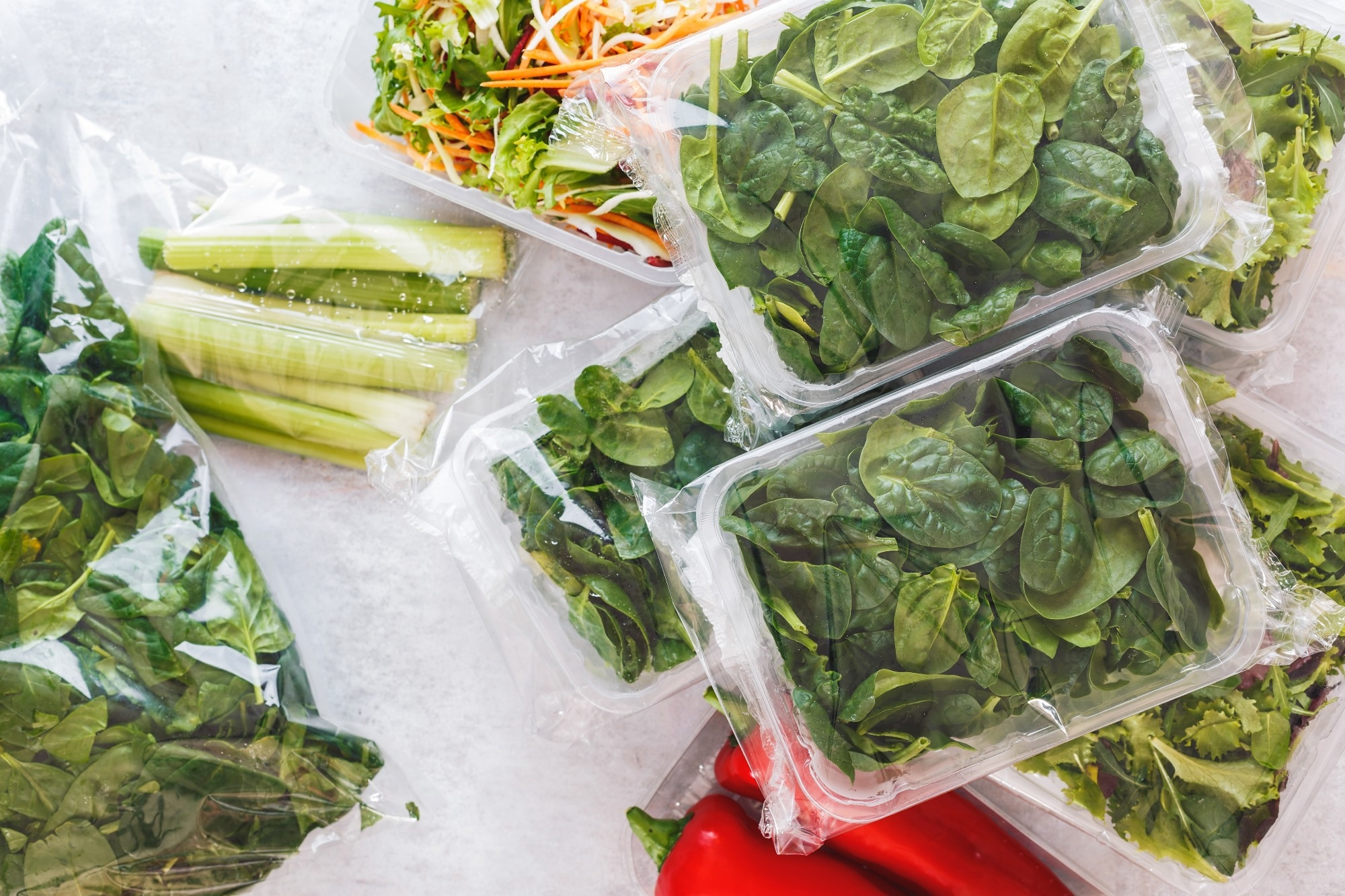 Birds eye image of salad leaves, celery, and spinach in plastic packaging.