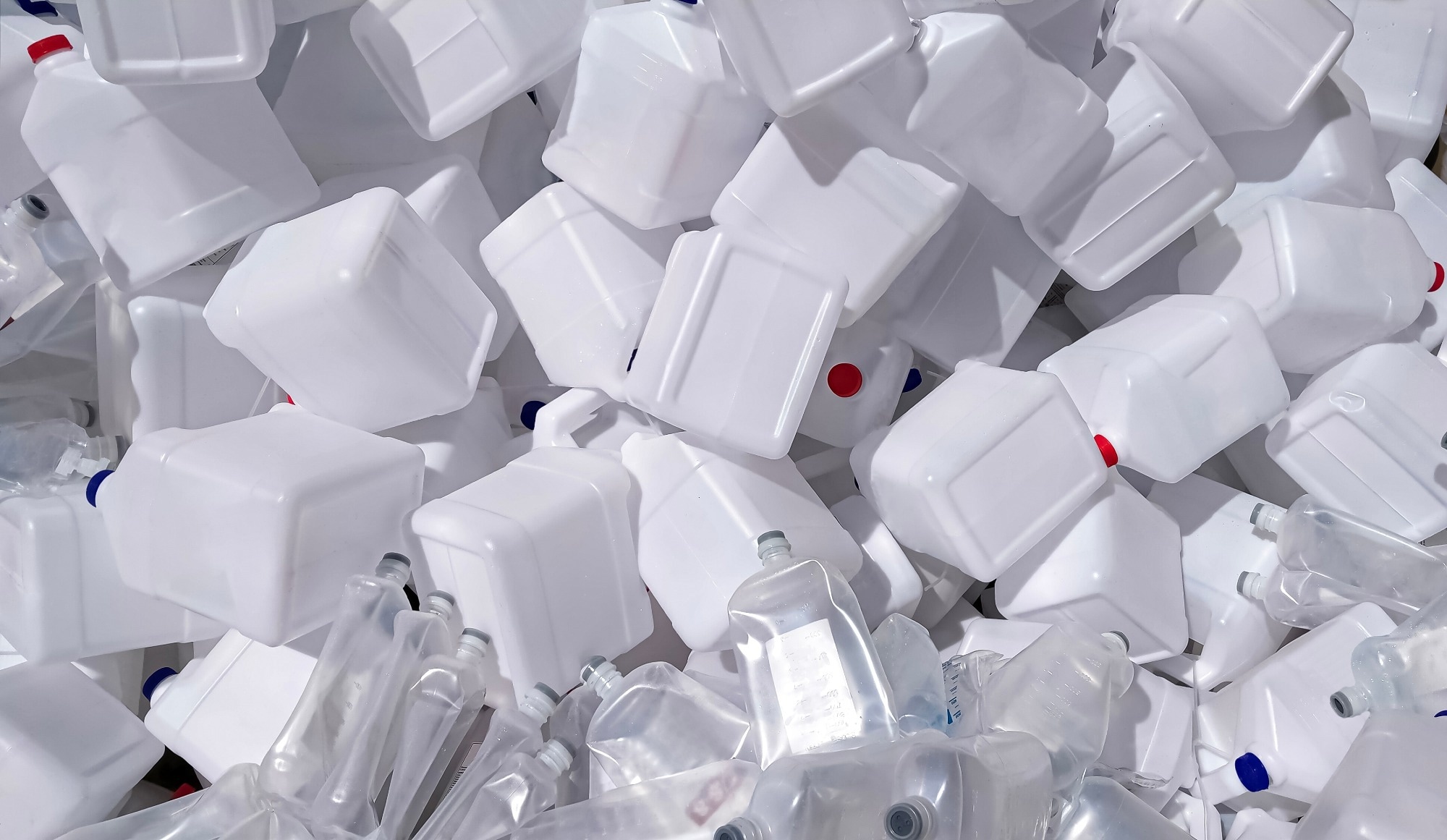 Pile of many white chemical plastic gallons and used saline solution bottles for recycling in hospital area