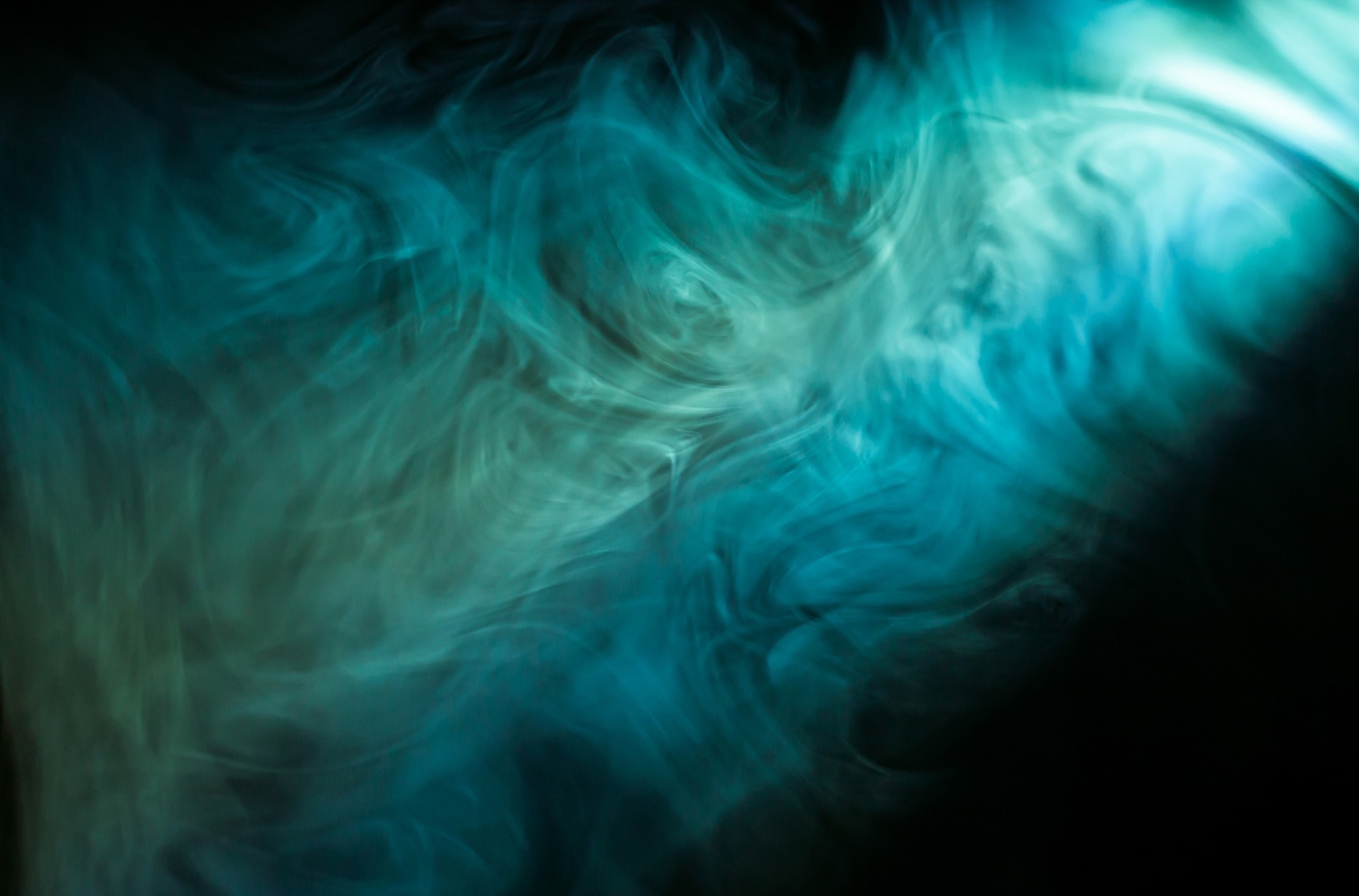 gas lit up by blue and green light swirls under a spotlight.